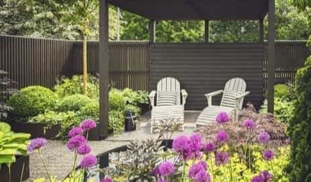 Twee ligstoelen onder een houten overkapping in de tuin met kleurrijke bloemen en planten.